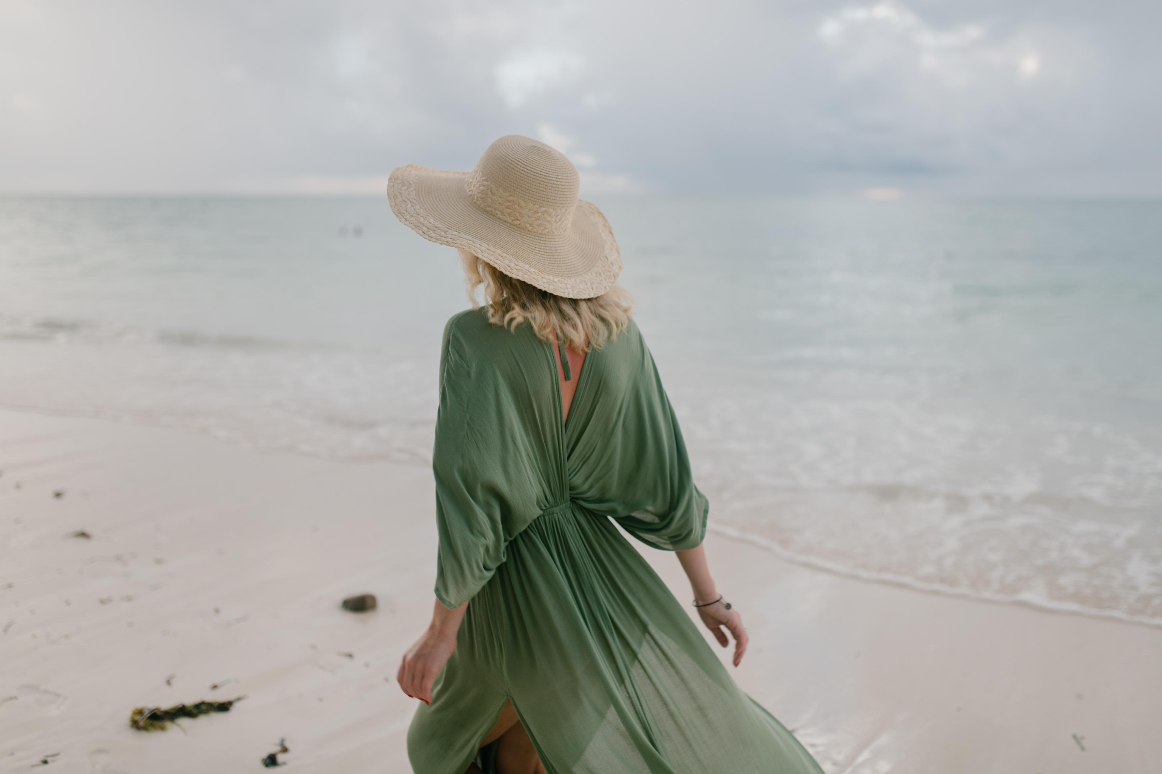 Woman in green dress walking away from camera on a beach.